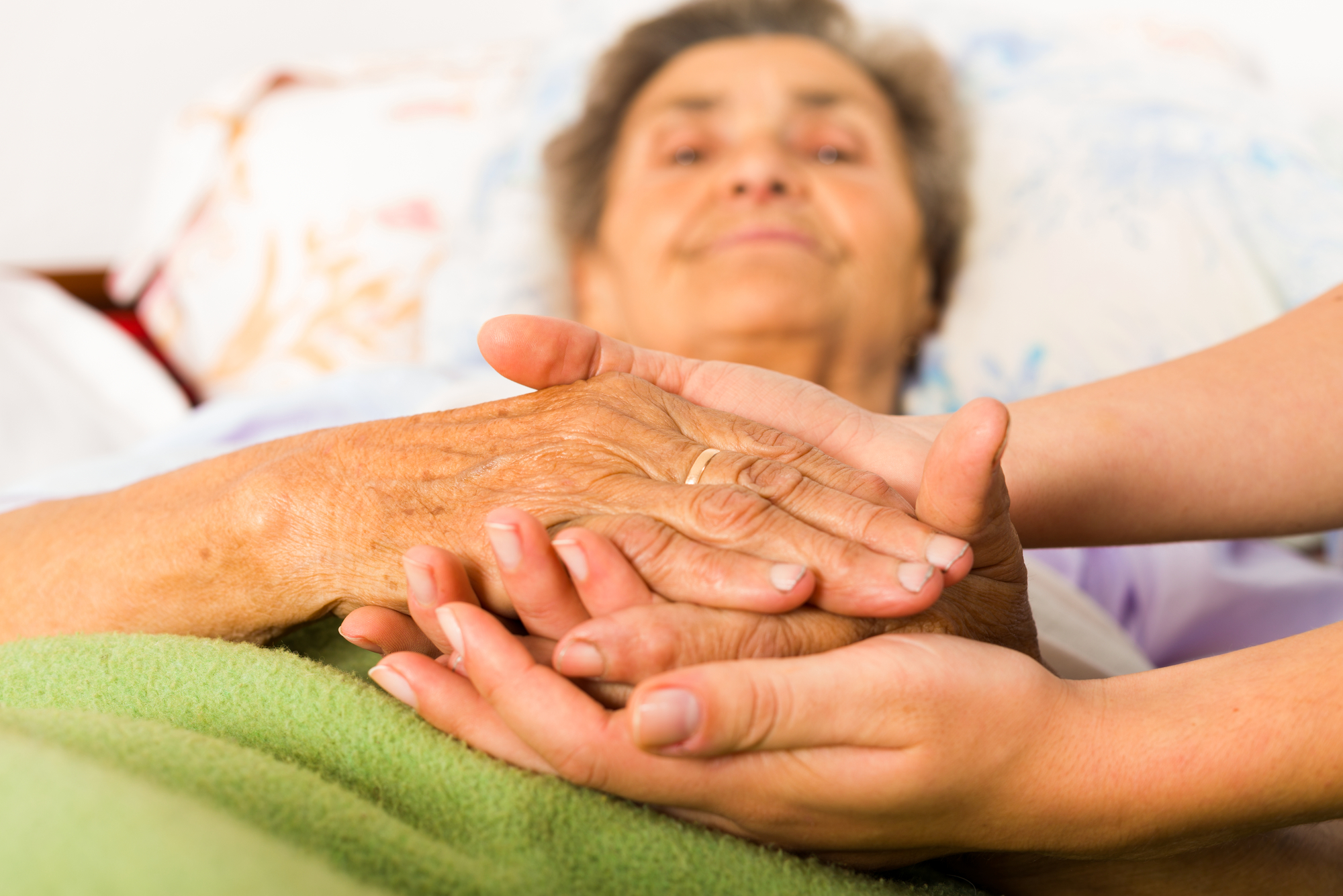 Caring nurse holding kind elderly lady's hands in bed.