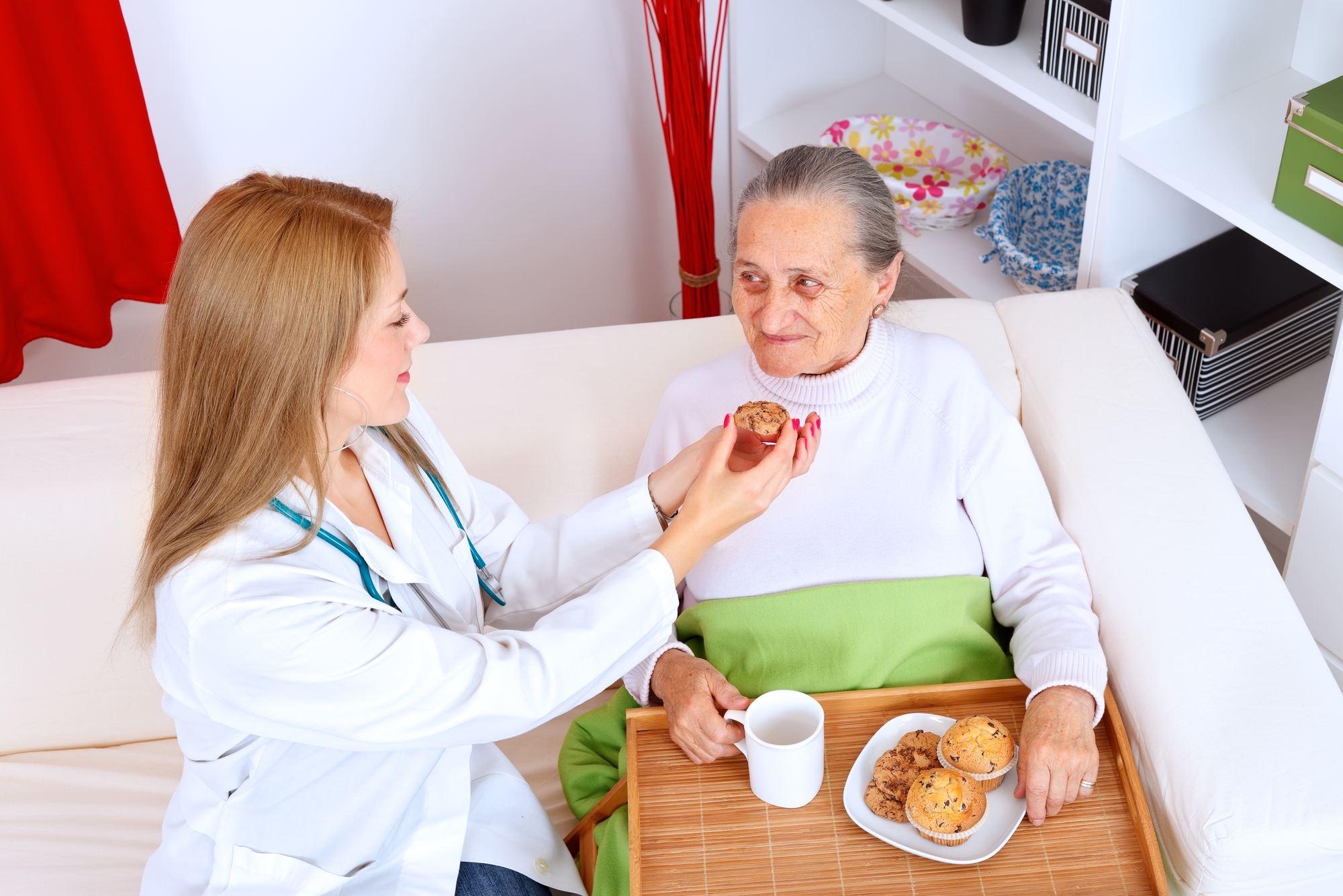 Lovely nurse helping old woman eating cookies