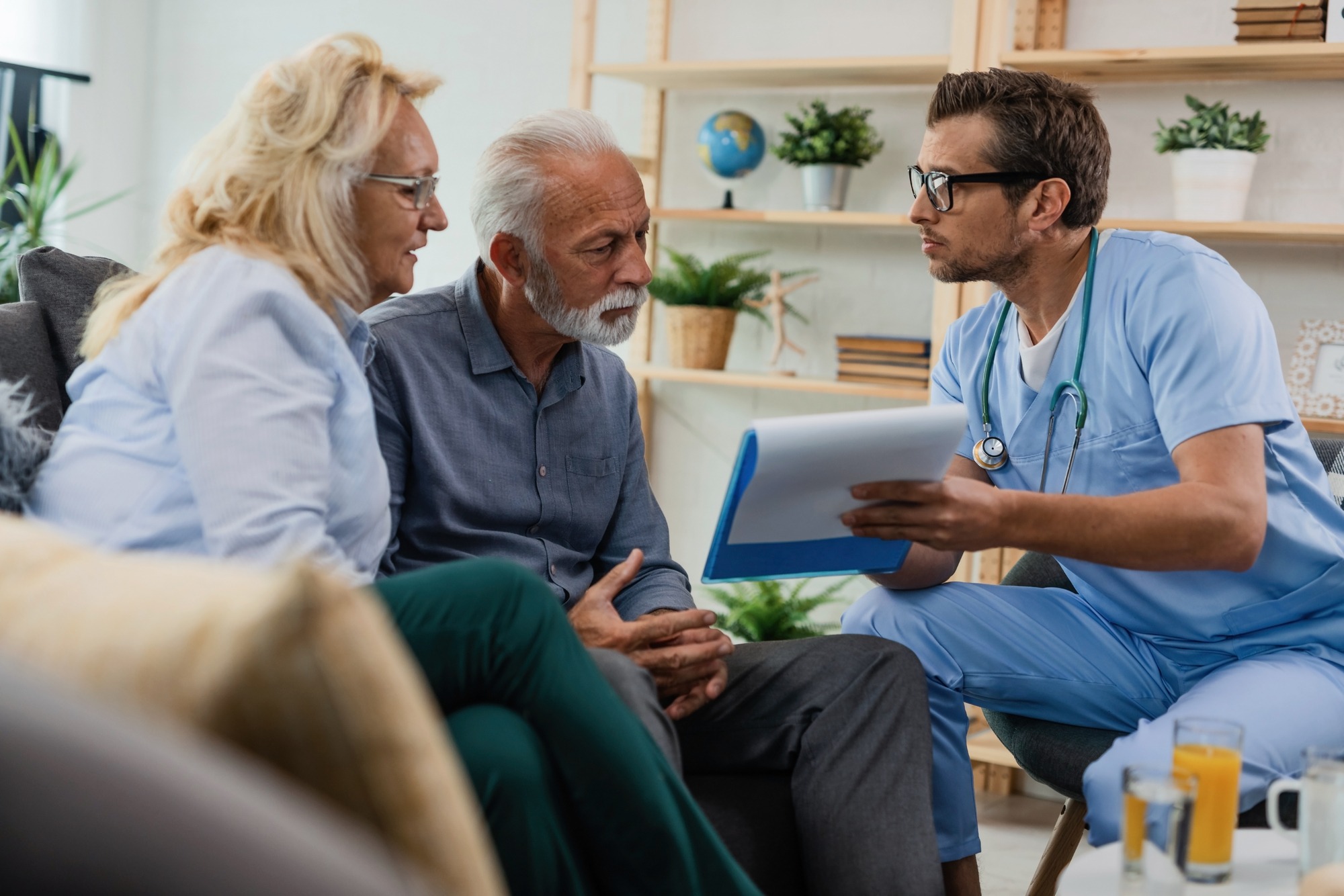 General practitioner showing to senior couple medical documents while being in home visit.